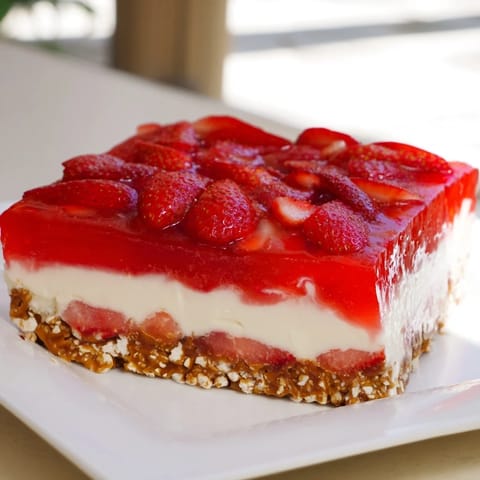 A cool slice of fresh Strawberry Pretzel Salad showing the creamy layers and bright red strawberries.