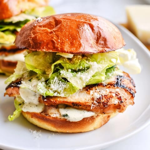 Grilled Caesar Chicken Sandwich garnished with Parmesan cheese and fresh tomato slices, ready to serve alongside golden fries on a wooden board.