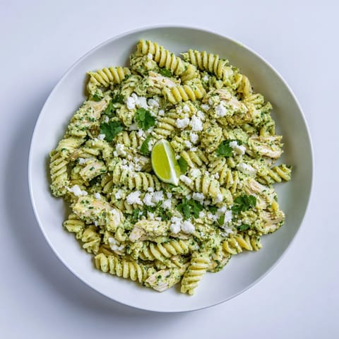 Creamy cilantro lime chicken pasta served in a white bowl with fresh lime wedges and crumbled feta.