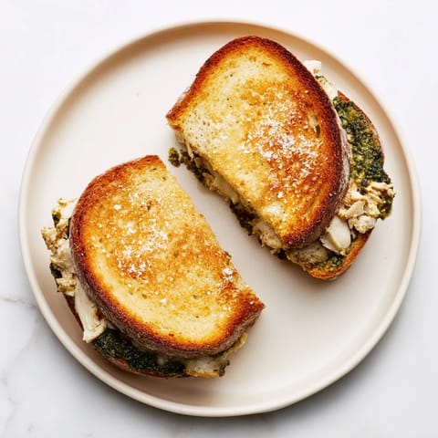 A close-up of Mozzarella Pesto Chicken Grilled Cheese with fresh basil leaves and juicy tomato slices inside.