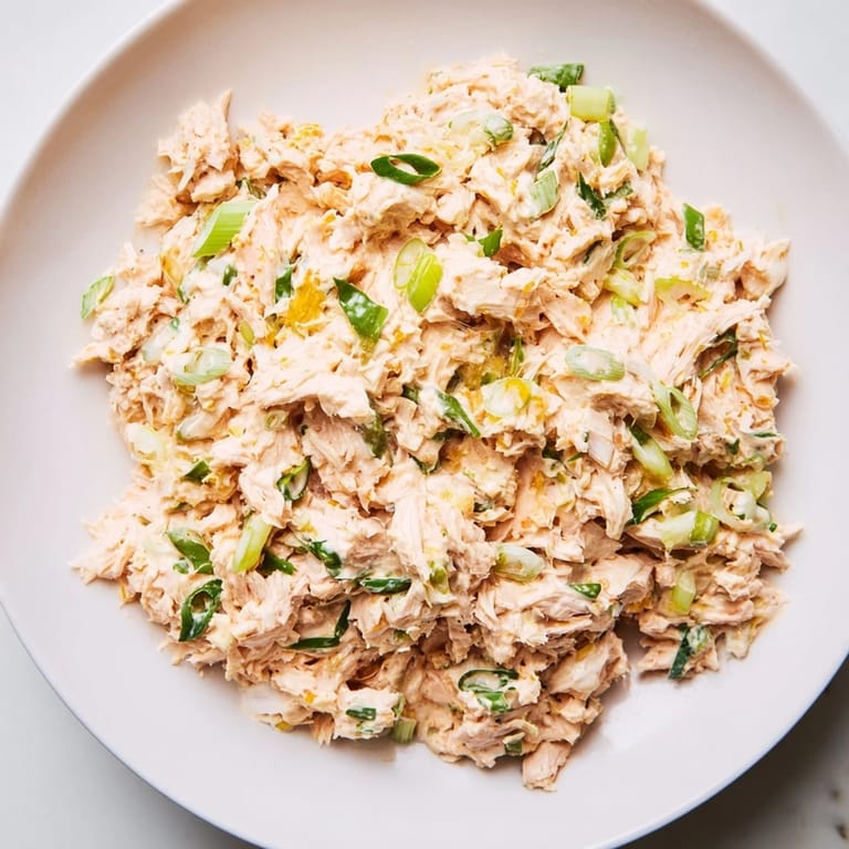 Bright, chilled spicy zesty tuna salad topped with scallions and celery, served on a rustic wooden table for a quick pescatarian lunch.