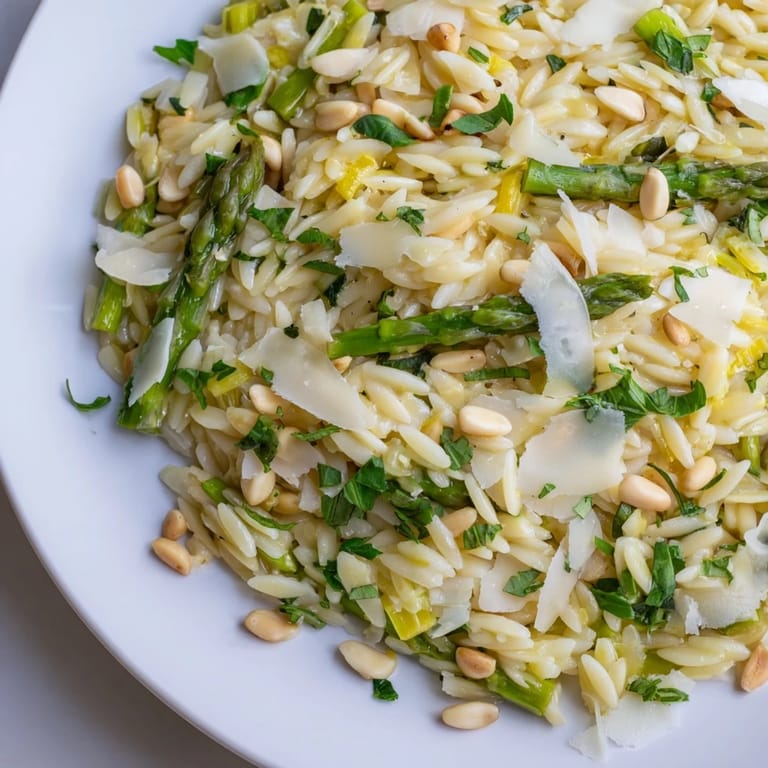 A close-up of a forkful of Asparagus Lemon Orzo Salad shows shaved asparagus, grated Parmesan, and a zesty lemon dressing drizzled over the pasta.