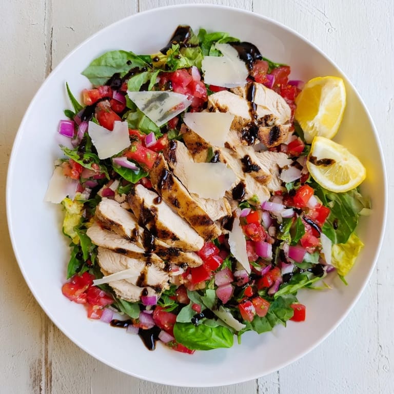 Bruschetta Chicken Salad served on a white platter, highlighting the colorful diced tomatoes, red onion, and fresh basil over warm grilled chicken slices, paired with lemon wedges for extra zest.