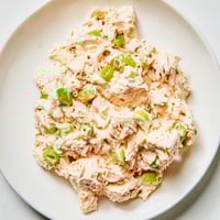 A close-up of spicy zesty tuna salad in a white bowl, garnished with fresh parsley and lemon wedges, ready for sandwiches or lettuce wraps.