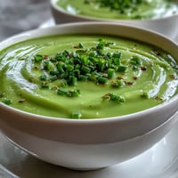Fresh pureed Asparagus Soup garnished with tender green tips and chives in a rustic white bowl, perfect for spring.