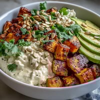 A colorful bowl of roasted sweet potatoes topped with creamy avocado, cottage cheese, and a spicy hot honey drizzle.
